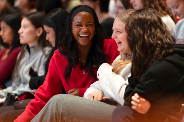 Three students seated in the crowd laugh together during the ceremony.