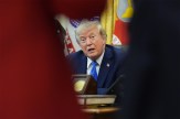 President Trump seated at the Resolute Desk, seen through the shoulders of two people in the foreground, mid-speech.
