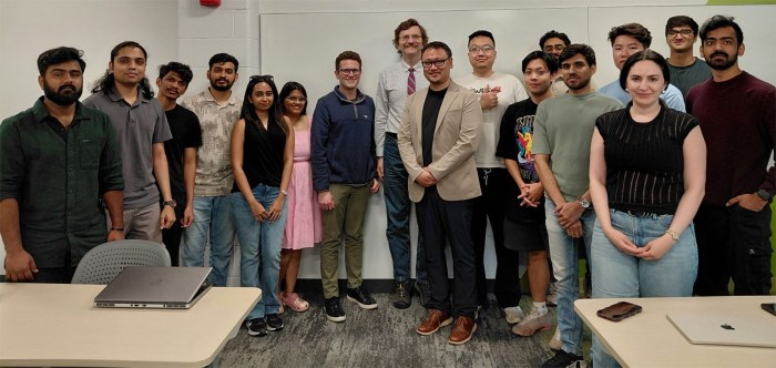 A group of about 15 students and faculty posing together in a classroom.