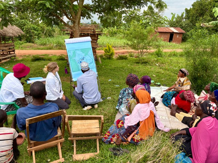 A crowd gathers to plan a community-project, with one person drawing out plans on a large canvas.