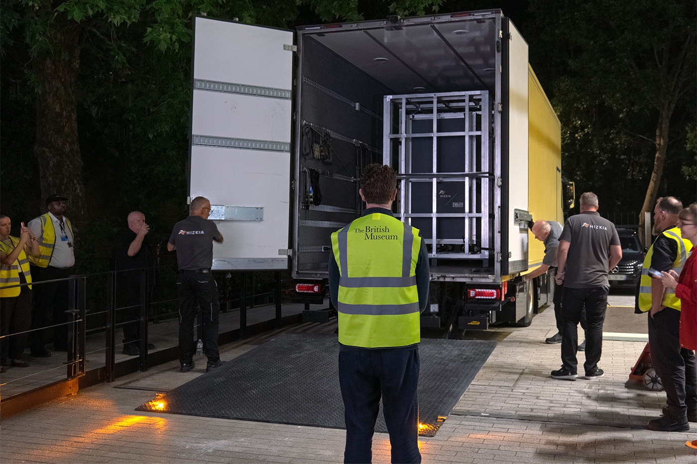 Crew members in hi-viz vests standing around the back of a truck carrying the Bayeux Tapestry to the British Museum.