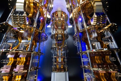 Gold-plated wiring and chandelier-like tiers of hardware descend from a central cryostat, lit against a dark background.
