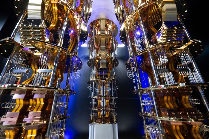 Gold-plated wiring and chandelier-like tiers of hardware descend from a central cryostat, lit against a dark background.