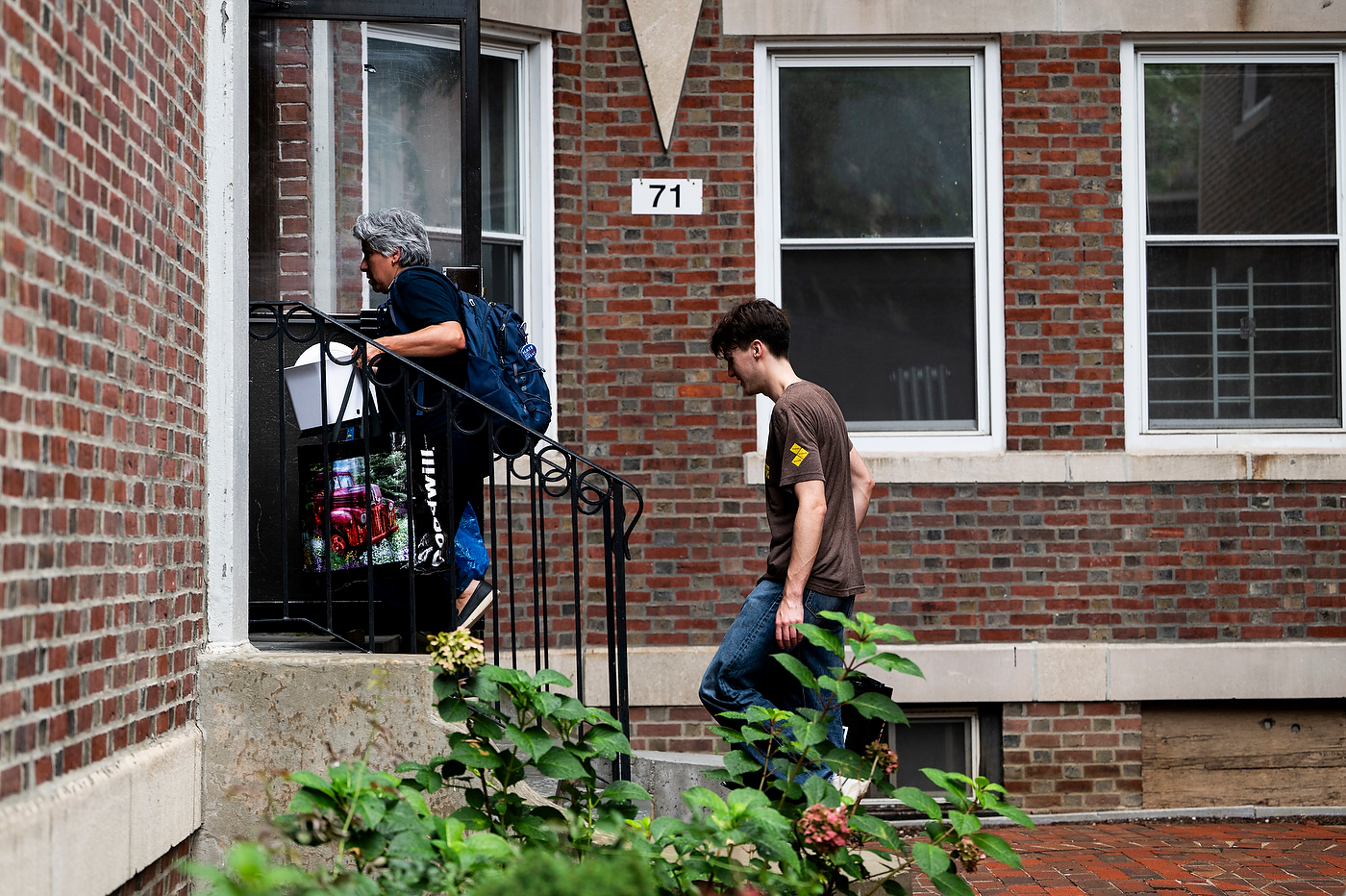 A student and his mother carry belongings into a brick off-campus apartment building. 