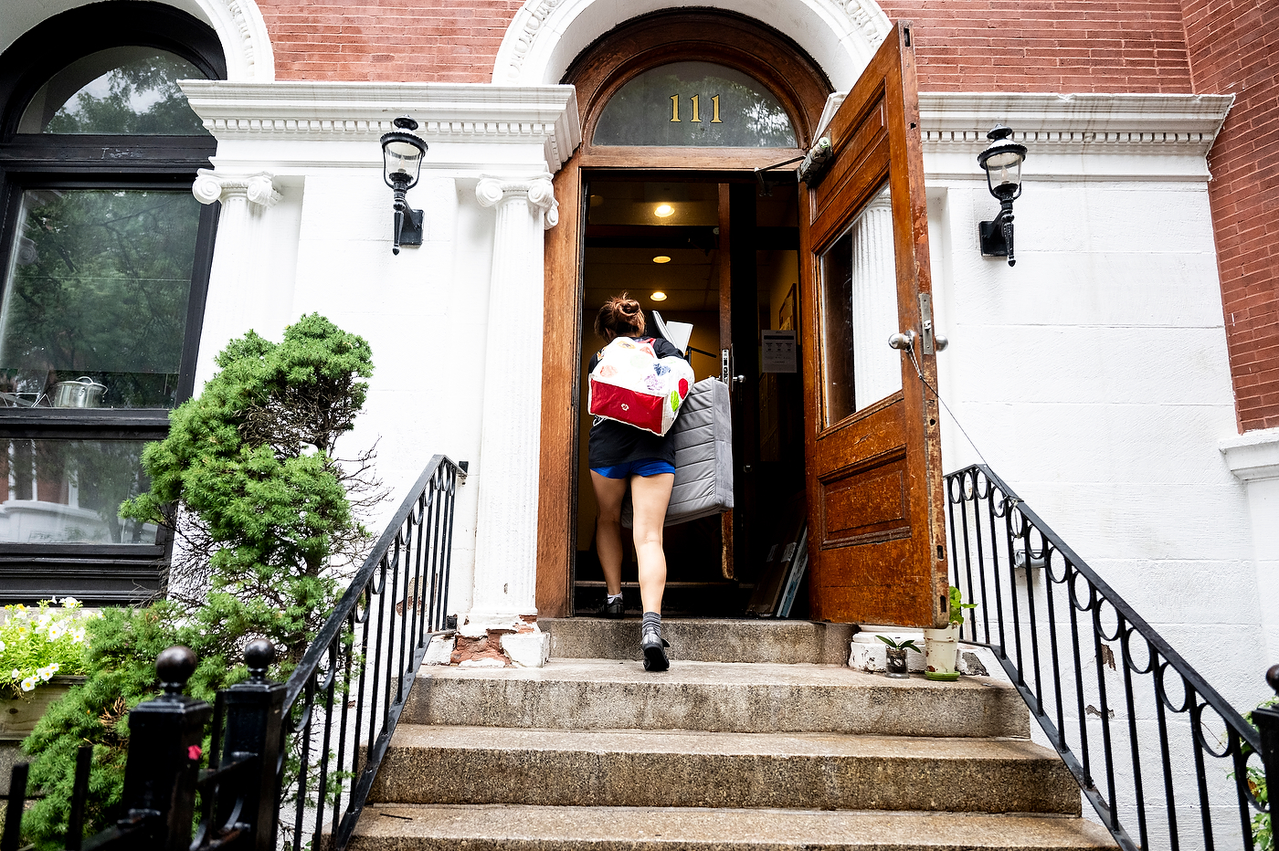 A person climbs up the stairs to an off-campus apartment carrying bags of stuff. 