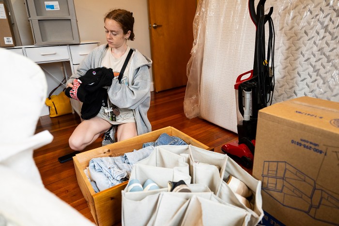 Student packing a shoe organizer and clothing into a wooden crate while moving into a dorm room