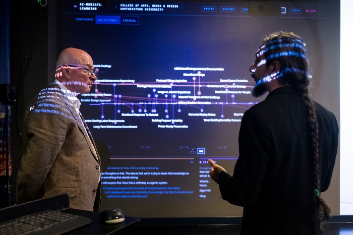 President Aoun and another man stand before a projected data visualization, both lit by the screen's glow.