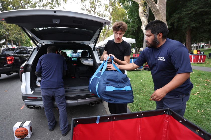 Two Northeastern move-in staff help a student unload a duffel bag from an SUV's open trunk.