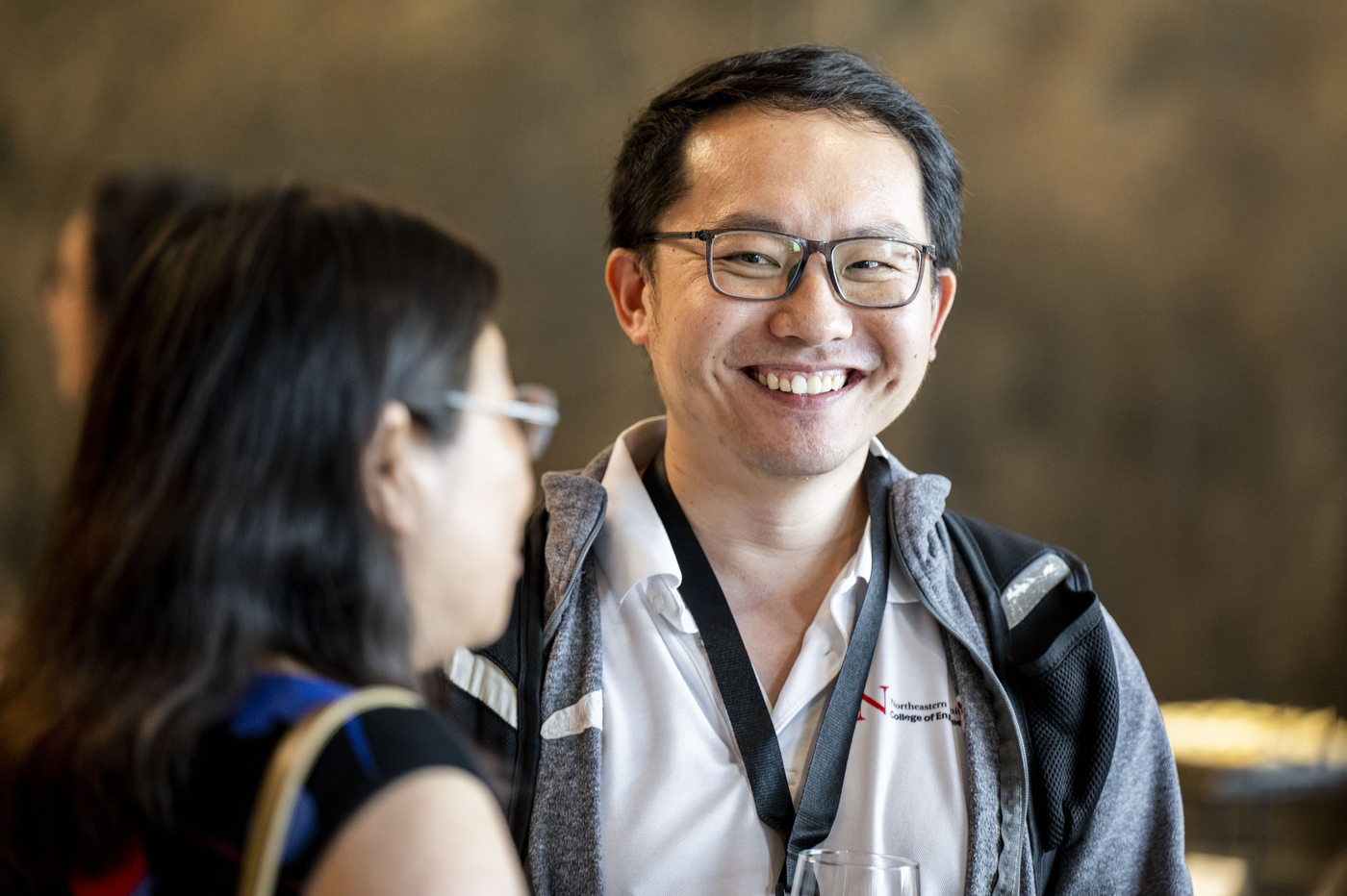 An attendee wearing a Northeastern College of Engineering shirt, smiling in conversation at the reception.