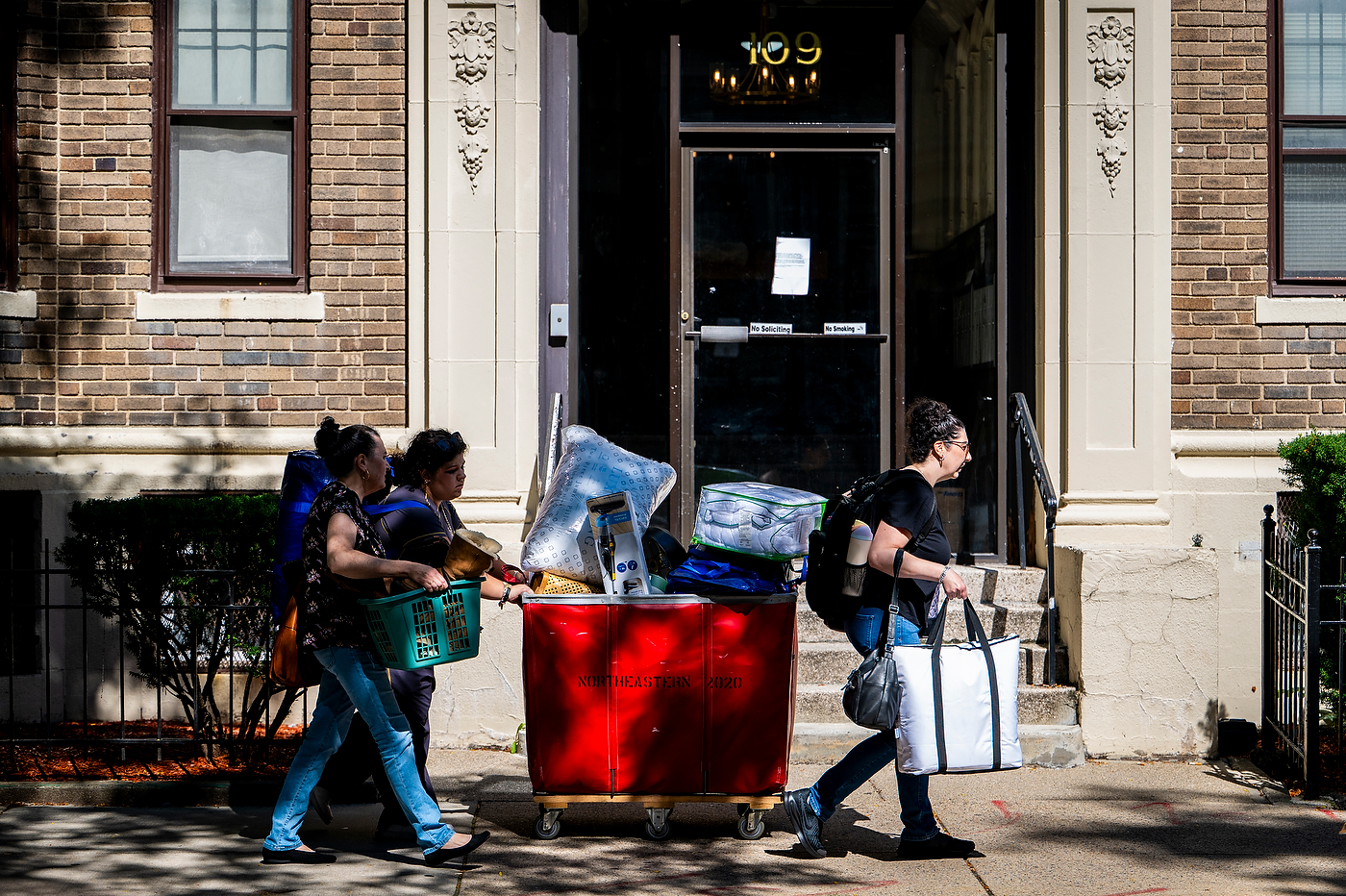 Students carry belongings past a brick residence hall entrance.