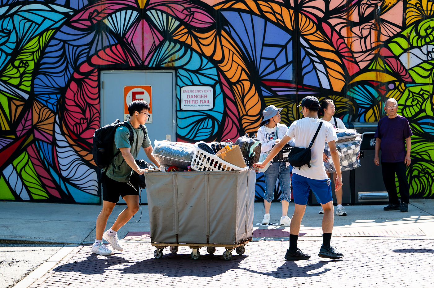 Students move a storage bin past a colorful mural.