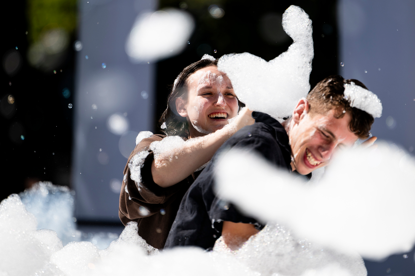 Two Northeastern students laugh and play in a cloud of foam during the Welcome Week BBQ on Centennial Common.
