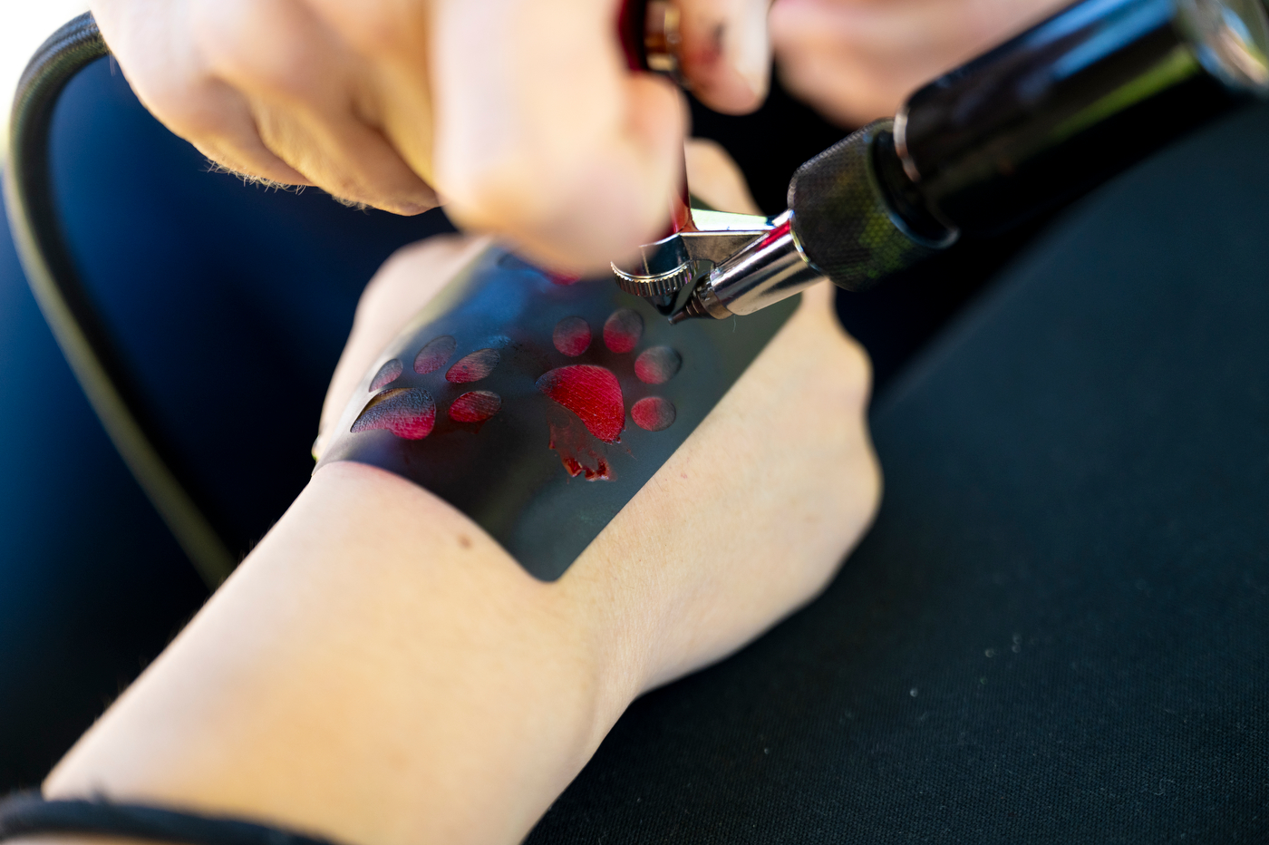 A close-up of a hand using a tool to decorate a forearm with red and black temporary body paint.