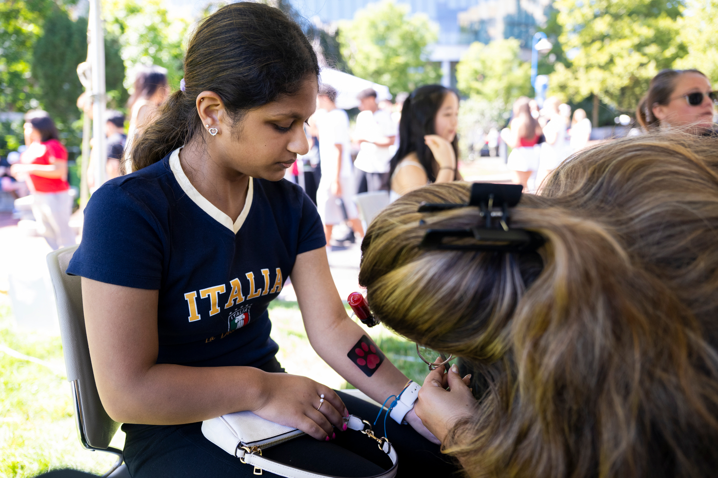 A Northeastern student looks down at a temporary tattoo on another student’s arm during the Welcome Week BBQ on Centennial Common.