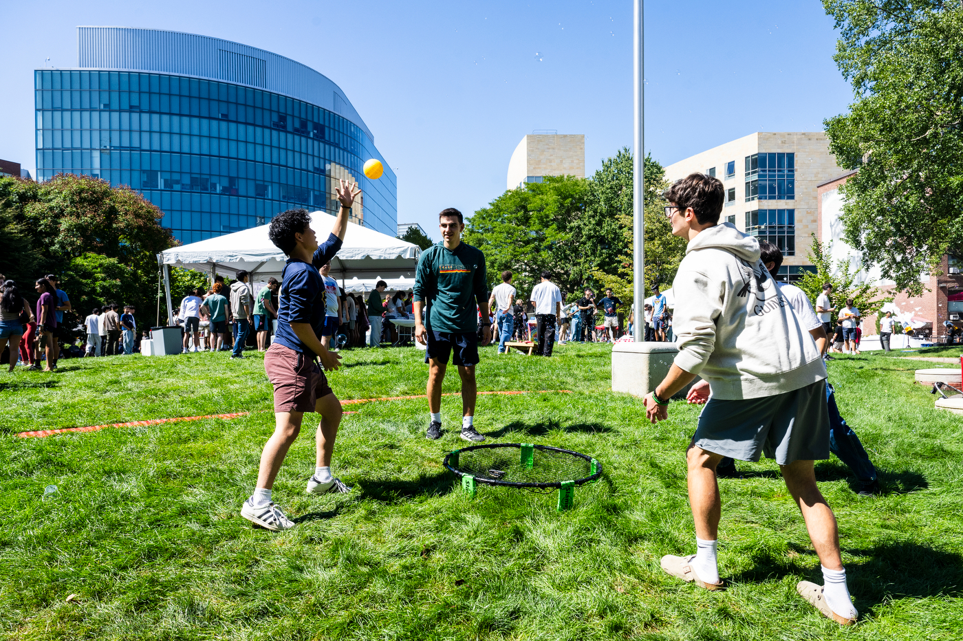 Northeastern students play with a yellow ball on Centennial Common during the Welcome Week BBQ, with campus buildings in the background.