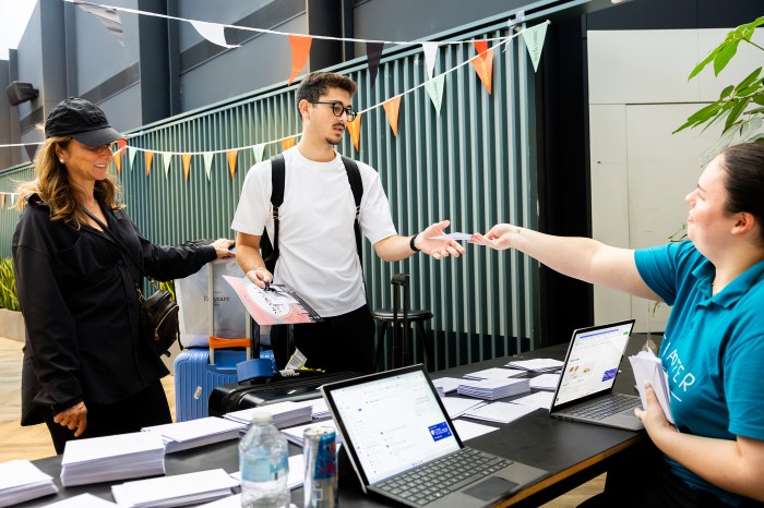 A student receives a keycard from a staff member at a check-in table decorated with pennant flags, with a family member standing beside him.
