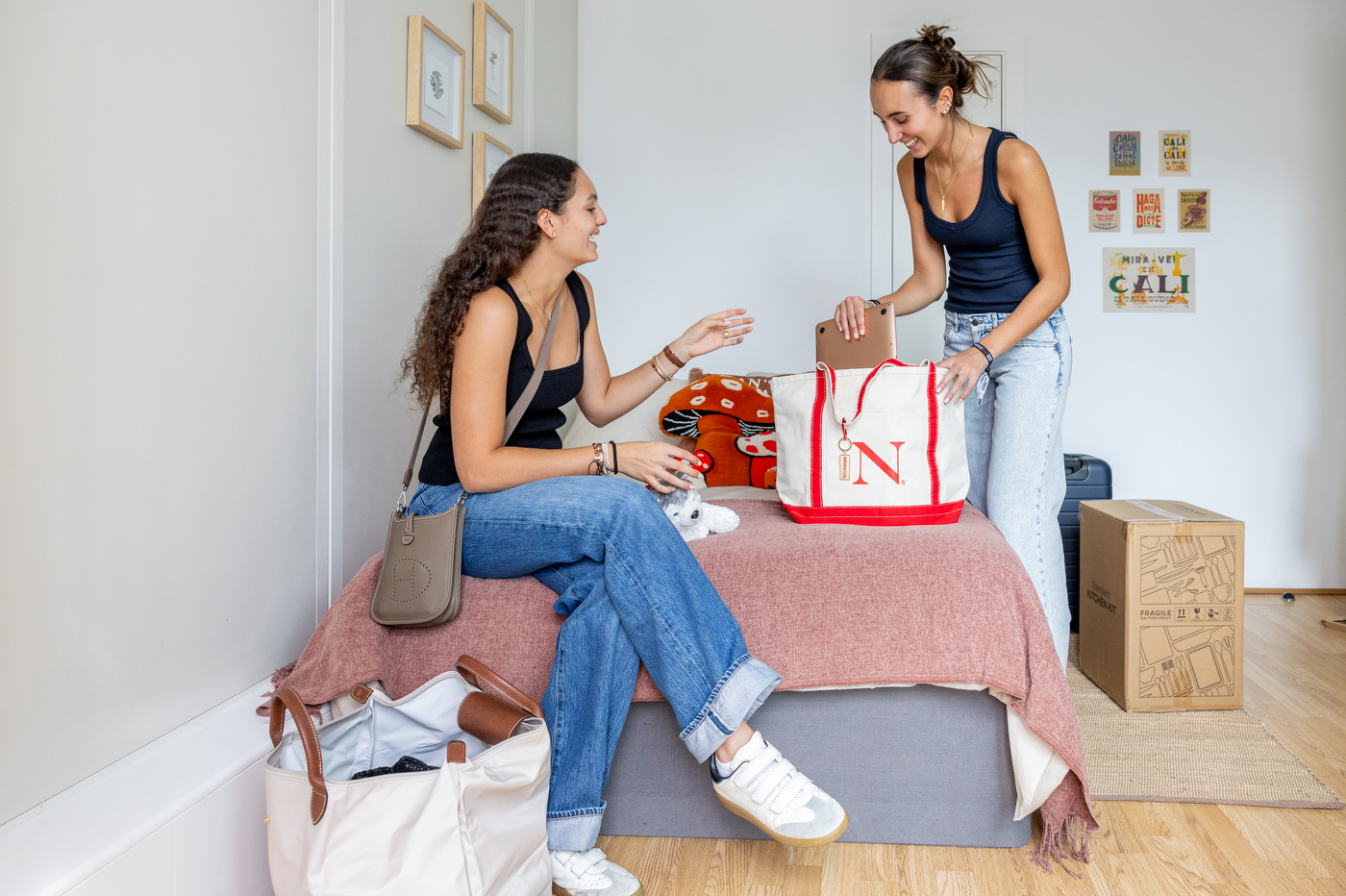 Two students unpack belongings on a bed in a London dorm room.