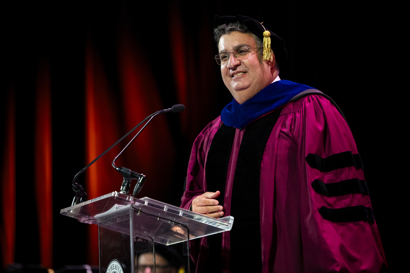 A Northeastern University faculty member in academic regalia speaks at the podium during the convocation.