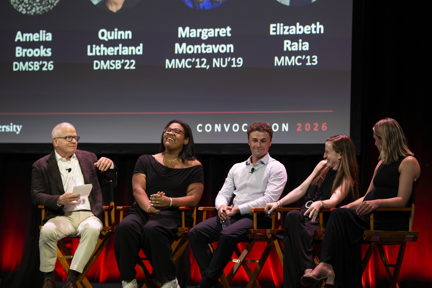A panel of Northeastern alumni and students takes part in a discussion onstage during the 2026 New York City convocation. A large screen behind them displays the panelists’ names and graduation years.
