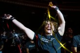 A Northeastern University student in a gray T-shirt raises both arms and smiles while holding metallic gold and red streamers during a lively event at The Town Hall in New York City. Other students stand in the dimly lit auditorium behind them.