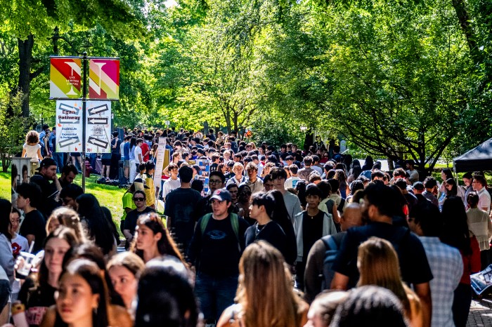 A dense crowd of students fills Egan Pathway, walking among club tables lining the path.