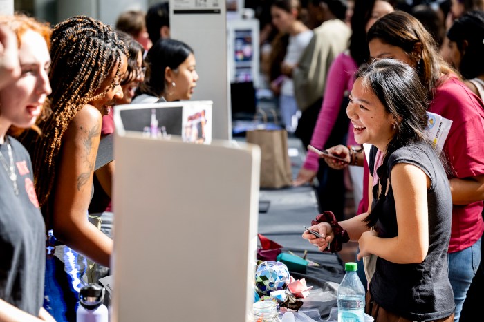 Students gather around a club fair table, browsing flyers and talking with representatives.