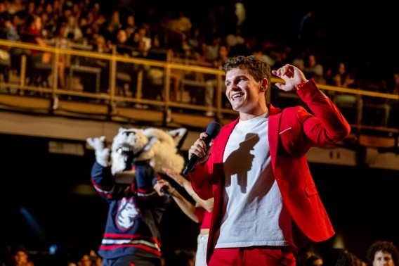 A student speaker with a microphone hyping up a crowd during the 2026 convocation. Paws is cheering in the background.