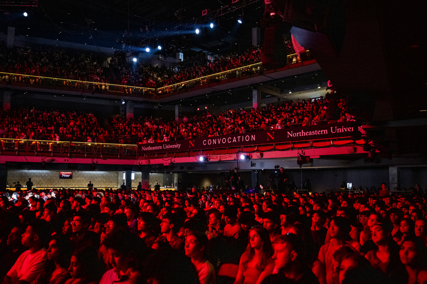 Wide view of a packed MGM Music Hall bathed in red lighting during the Boston Convocation ceremony