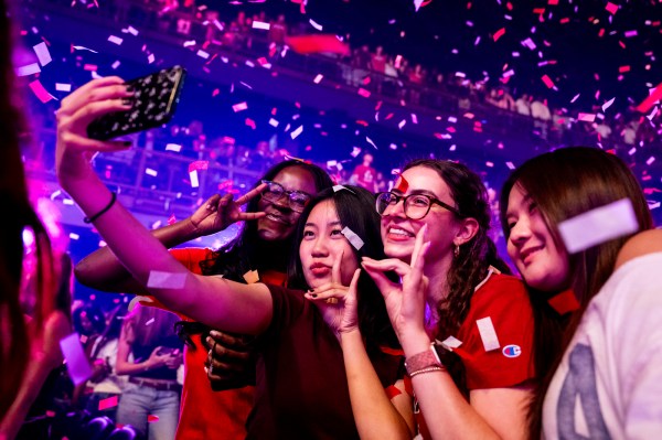 Students take a selfie amid falling confetti, smiling and posing with peace signs.