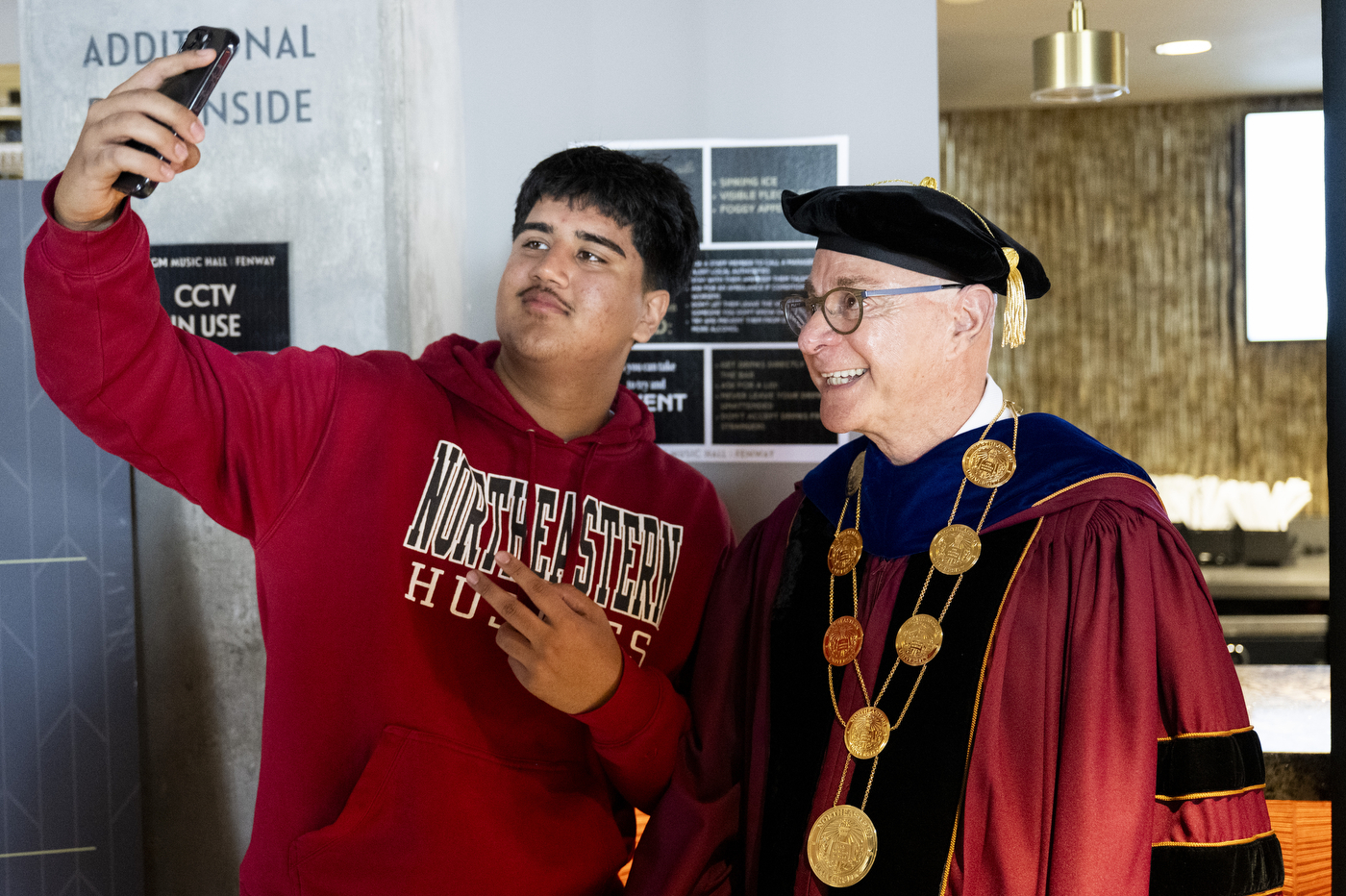 Student takes a selfie with President Aoun in academic regalia.