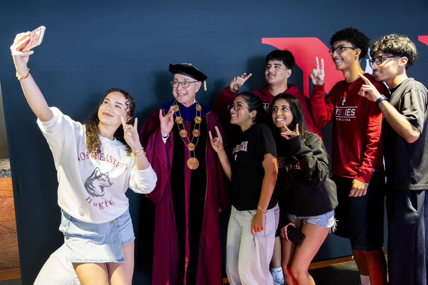 President Aoun in regalia poses with a group of students for a selfie.