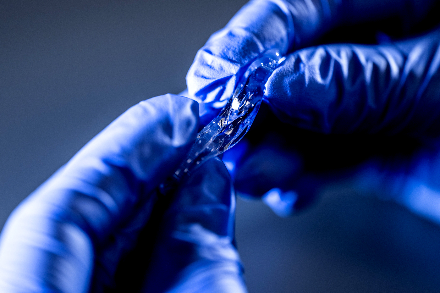 Gloved hands stretching a translucent strip of hydrogel until it thins into a delicate strand.