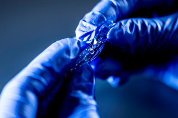 Gloved hands stretching a translucent strip of hydrogel until it thins into a delicate strand.