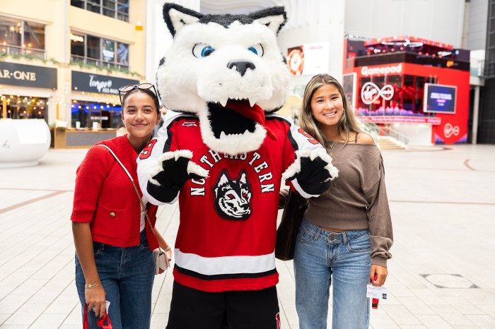 Two students pose with Northeastern's Paws mascot outdoors