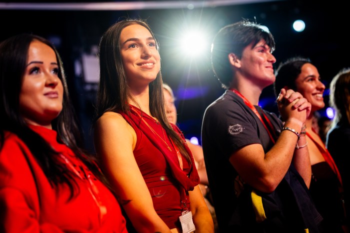 Students in Northeastern attire smile and look toward the stage