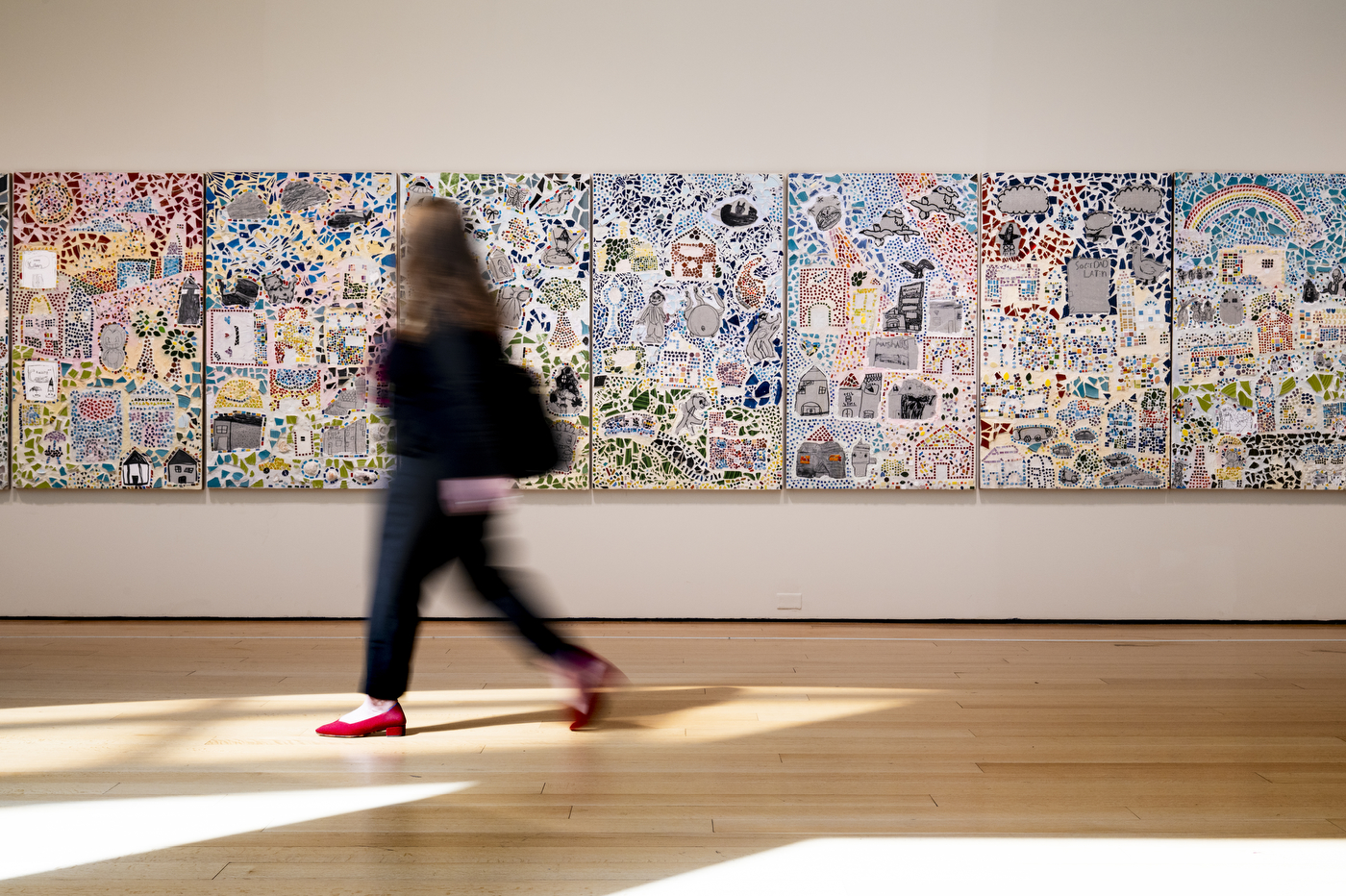 A person walks past a wall of art exhibits.