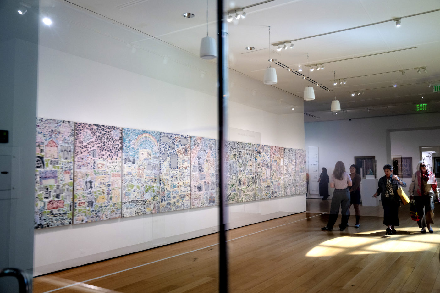 Visitors walk through a gallery lined with large mosaic murals at the "Can You Hear the City?" exhibit at the MFA.