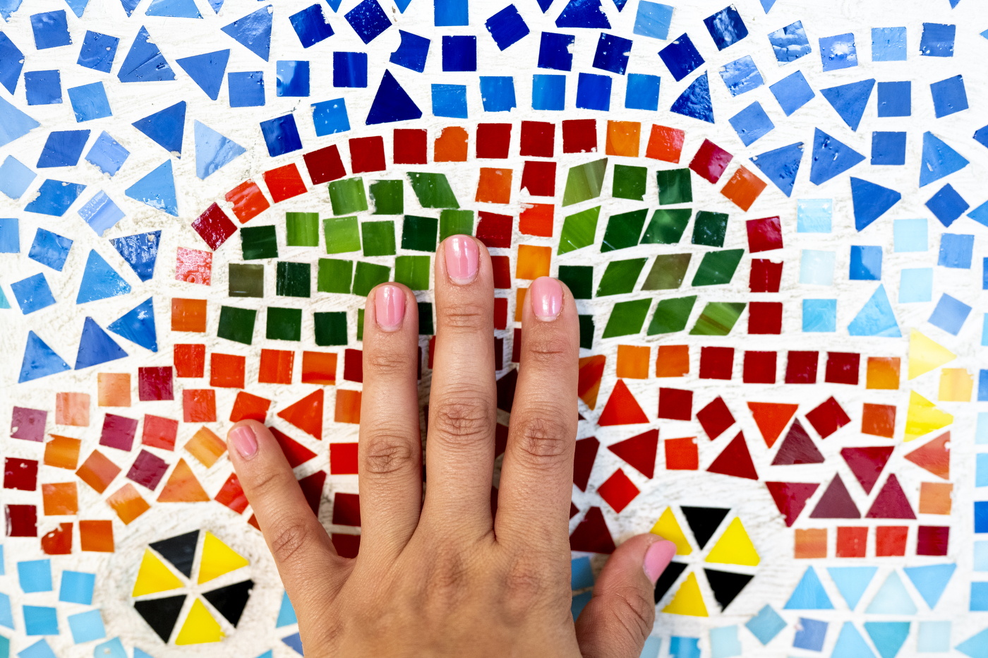 A close up of a hand on a wall of colorful mosaics.