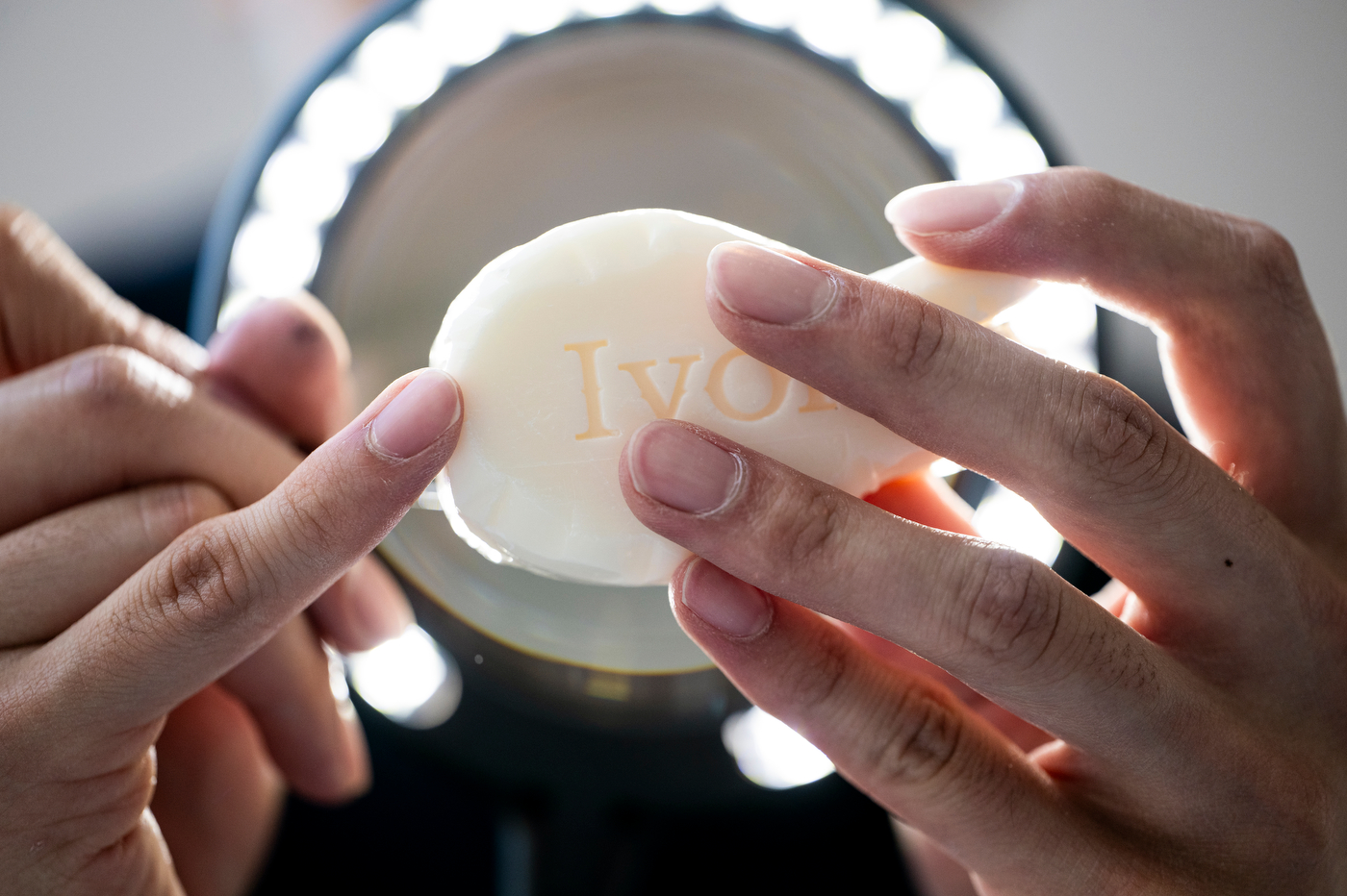Close-up of hands shaping a round bar of Ivory soap with a carving tool.