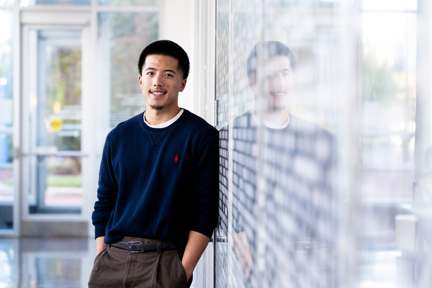 Aaron Tran, founder of Northeastern's Soap Carving Club, poses in a glass-walled hallway on campus.