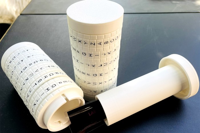 A cylindrical cipher device with rows of letters printed on rotating bands, disassembled to show its interior components.