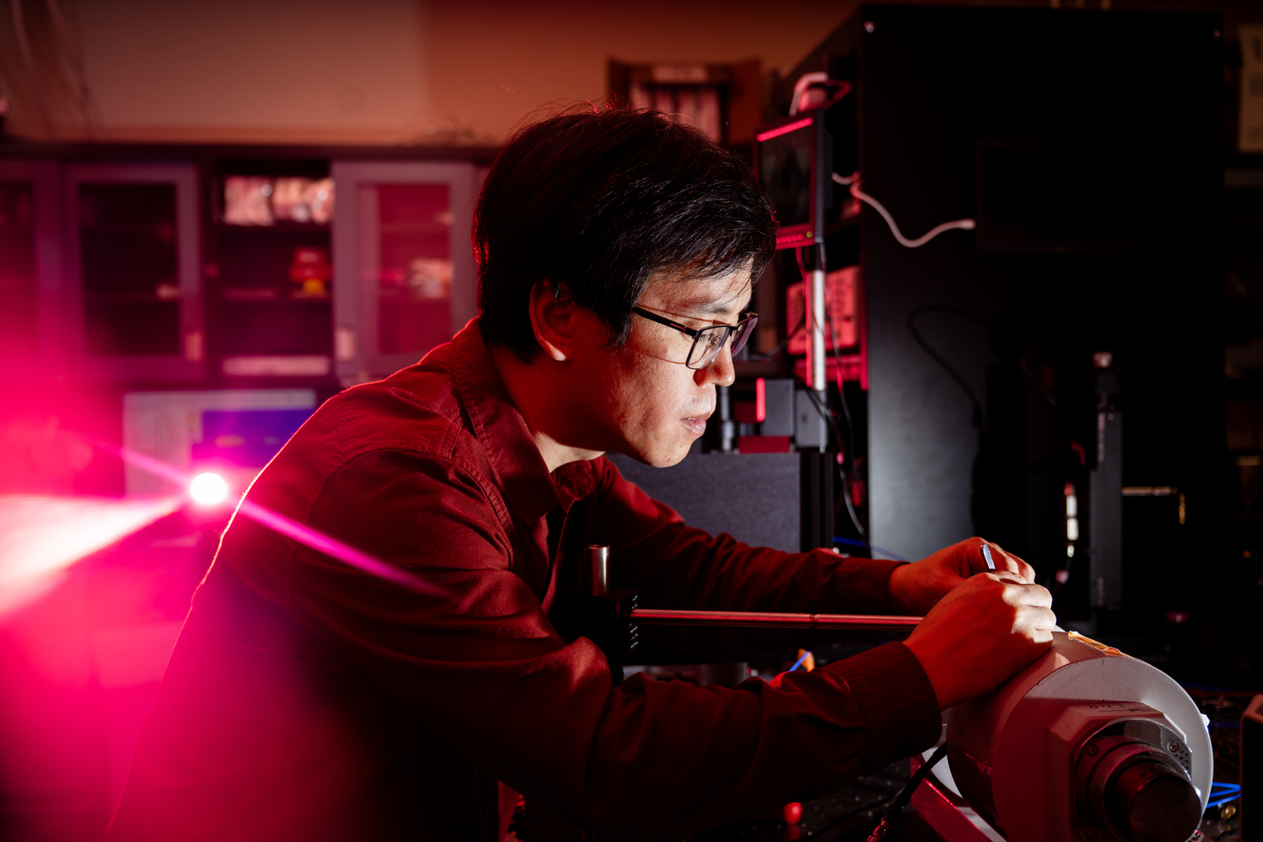 Xufeng Zhang works in a lab, illuminated in pink light.