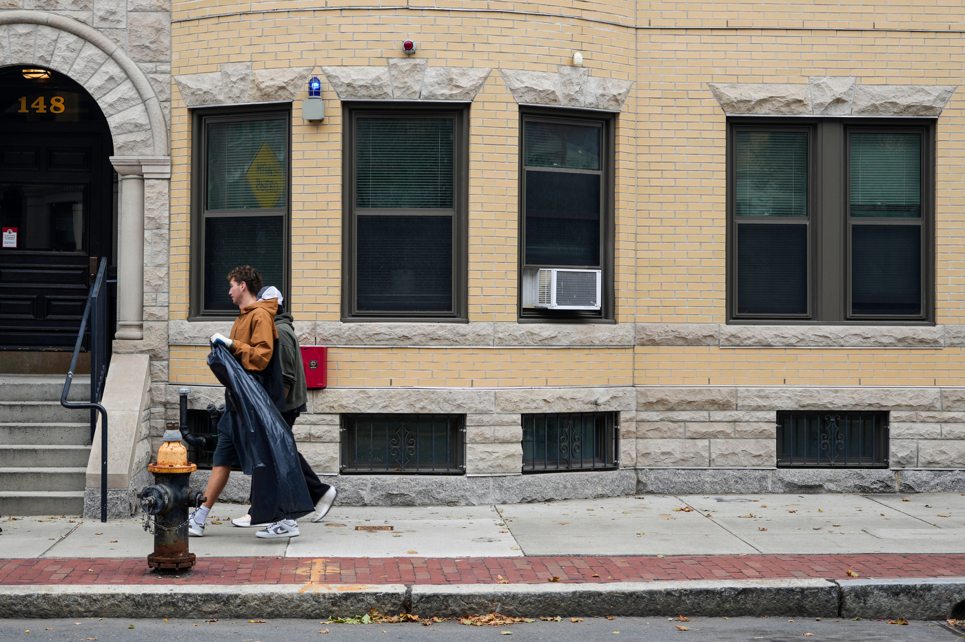 A student walks down the street holding a black plastic bag to collect trash.