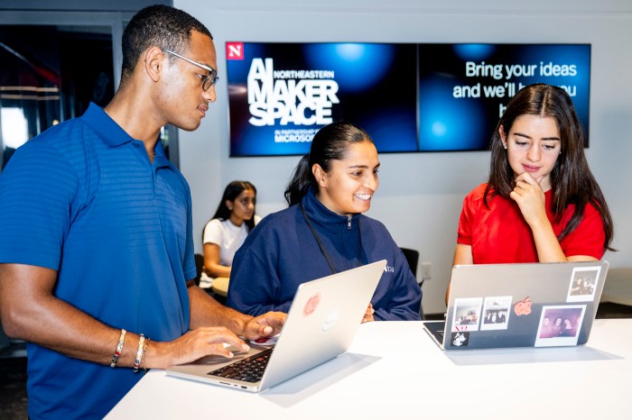 A student speaking with two seated students working on laptops in the AI Makerspace, with screens in the background reading "Bring your ideas and we'll..."