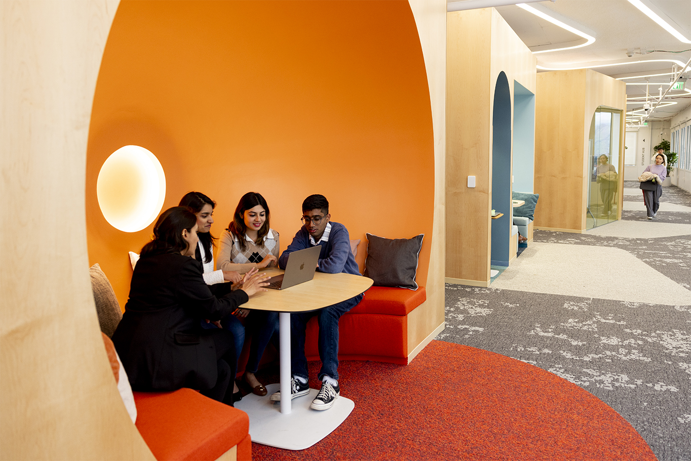 Four students gather around a laptop in an orange seating alcove off a hallway at Northeastern’s Silicon Valley campus.