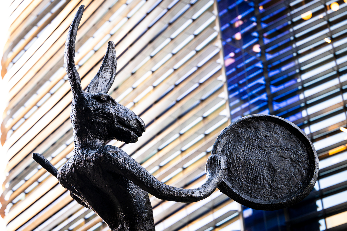 Close-up of the bronze hare's head, long ears and outstretched arm holding a round drum.