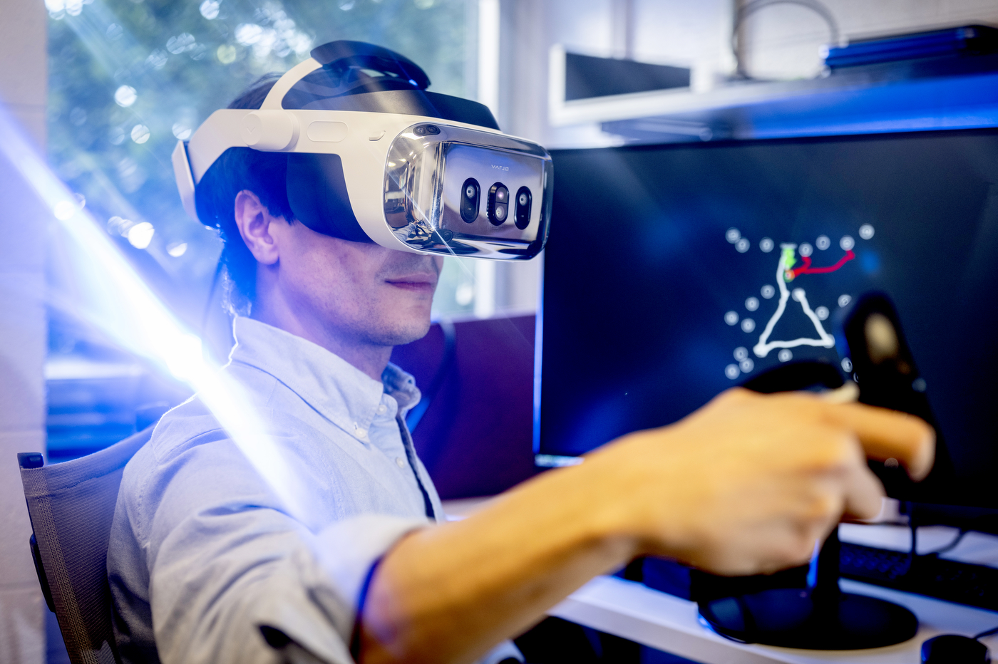 Quentin Coppola wearing a virtual reality headset and holding a controller in front of a monitor showing a line drawing similar to connect-the-dots. 