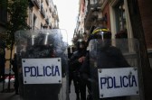 Police in riot gear caay shields that say "Policia" in a European city.